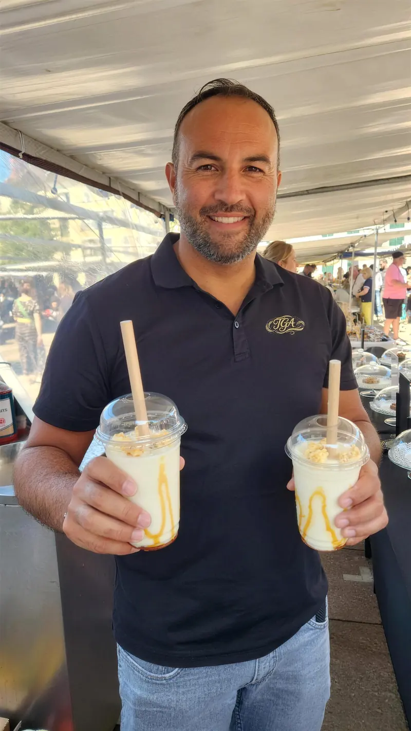 Alexandre souriant, un milkshake dans chaque main, au marché.