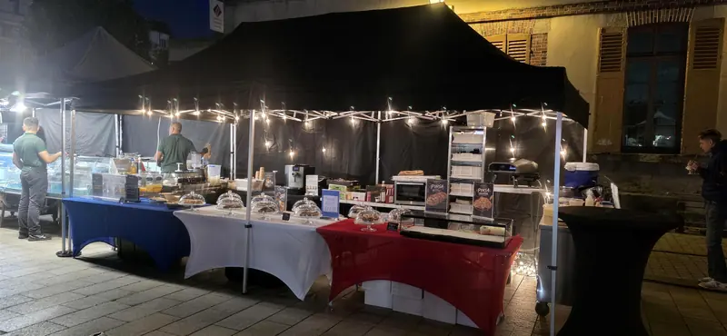 Le stand Tendances Gourmandes d’Alex de nuit, sous un barnum noir éclairé de guirlandes.